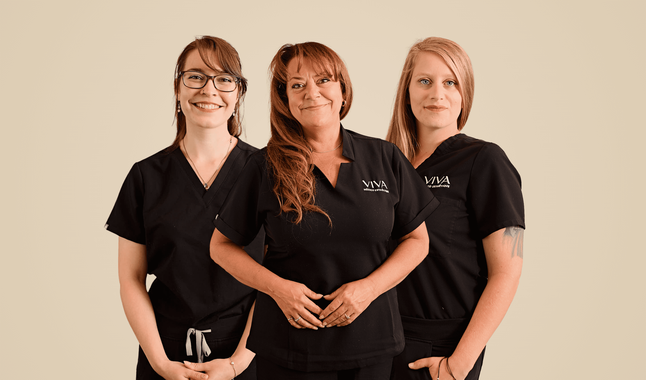 Trois femmes portant des blouses noires se tiennent ensemble, souriant à l'appareil photo sur un fond beige uni. Les deux femmes sur les côtés ont les mains devant elles, tandis que la femme au centre a les mains jointes.