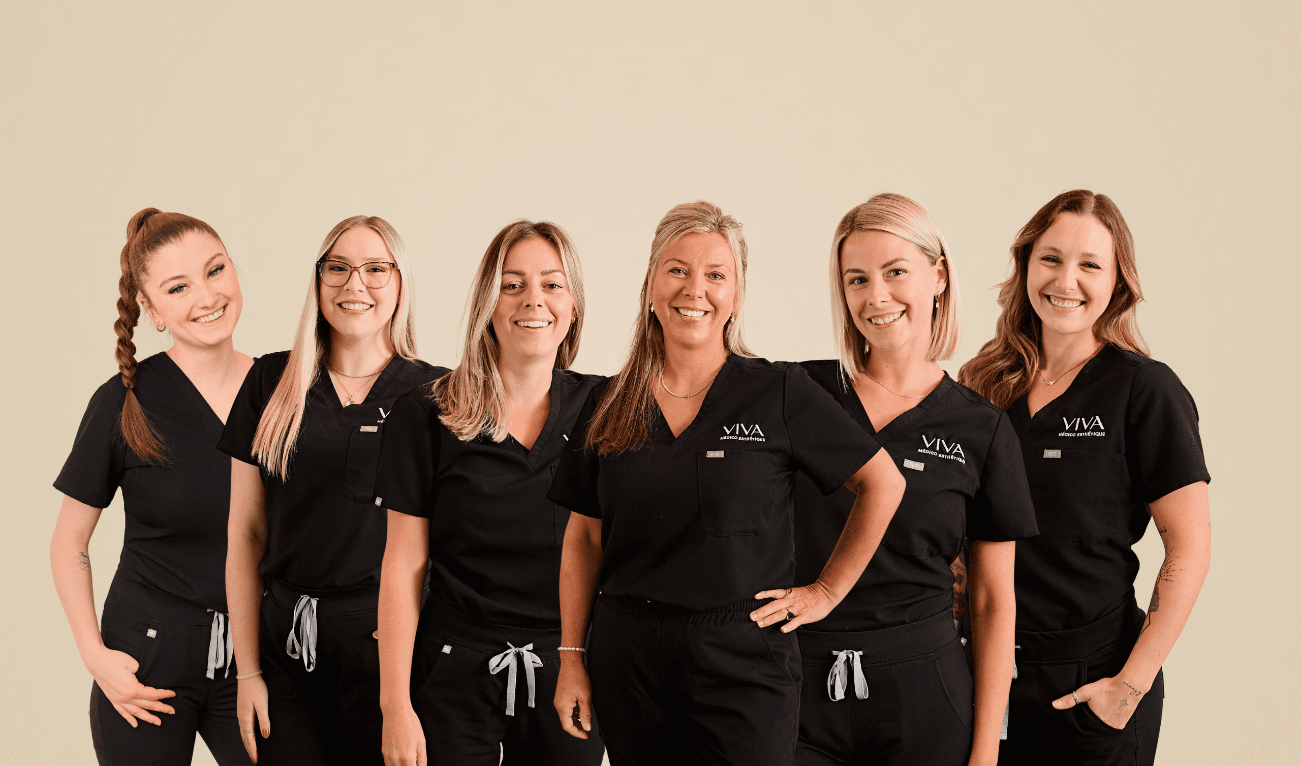 Six femmes portant des blouses médicales noires se tiennent ensemble, souriantes, sur un fond beige uni.